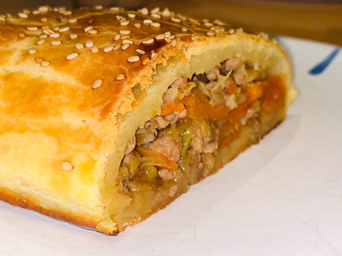 Angeschnittener Krautstrudel mit Sesam und sichtbarer Kraut-Fleisch-Füllung mit Karotten